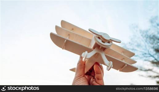 Freedom concept, human hand holding wooden plane on the sunset sky background