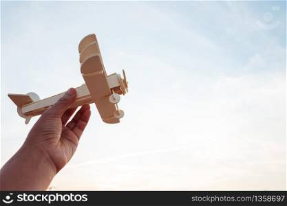 Freedom concept, human hand holding wooden plane on the sunset sky background