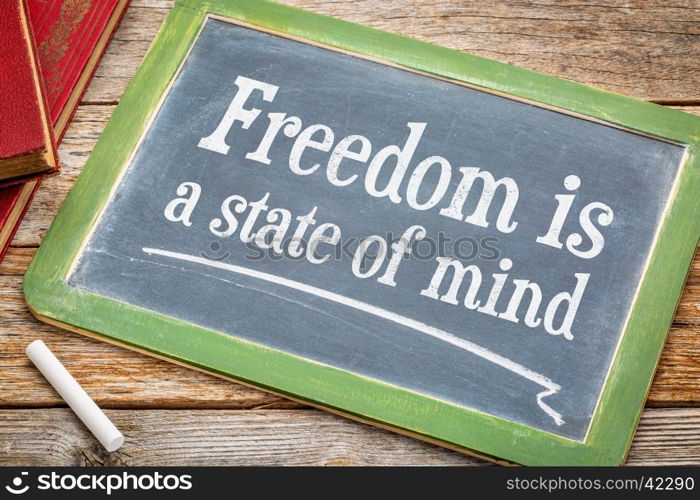 freedom is a state of mind - inspirational text on a slate blackboard with a white chalk and a stack of books against rustic wooden table