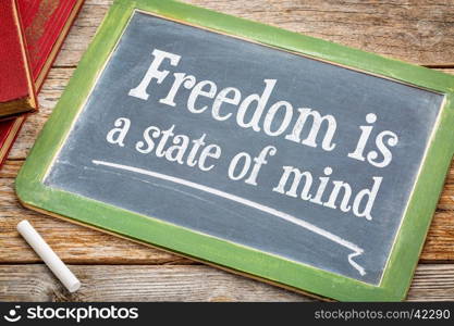 freedom is a state of mind - inspirational text on a slate blackboard with a white chalk and a stack of books against rustic wooden table