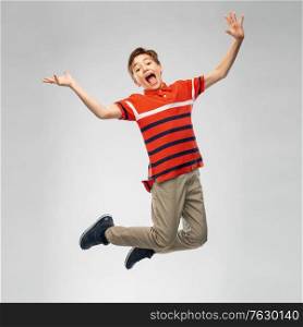 freedom, motion and happiness concept - happy smiling young boy jumping in air over grey background. happy smiling young boy jumping in air
