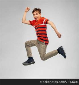 freedom, motion and happiness concept - happy smiling young boy jumping or running in air over grey background. happy smiling young boy jumping or running in air