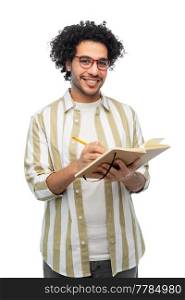 freedom, motion and happiness concept - happy smiling young man in glasses with diary and pencil writing over white background. happy smiling young man with diary and pencil