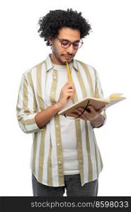 freedom, motion and happiness concept - thinking young man in glasses with diary and pencil writing over white background. thinking young man with diary and pencil