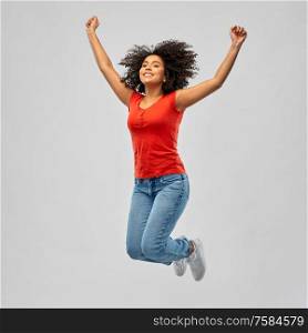freedom, motion and people concept - happy smiling african american young woman jumping in air with raised arms over grey background. smiling african american woman man jumping in air