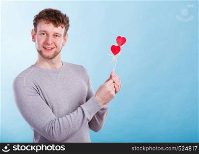 Freedom of feelings. Young happy smiling man with little red hearts on sticks. Romantic man dreaming of his love relationship.. Man in love with hearts.