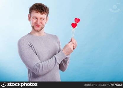 Freedom of feelings. Young happy smiling man with little red hearts on sticks. Romantic man dreaming of his love relationship.. Man in love with hearts.