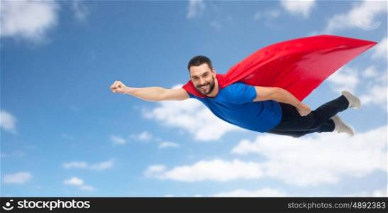 freedom, power, motion and people concept - happy man in red superhero cape flying over blue sky and clouds background