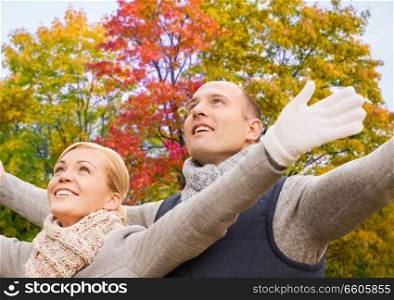 freedom, season and people concept - happy couple spreading hands over autumn park background. happy couple spreading hands leaves in autumn park