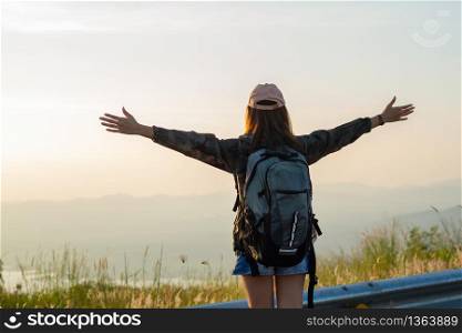 Freedom traveler woman standing with raised arms and enjoying a beautiful nature and cheering young woman backpacker at sunrise seaside mountain peak