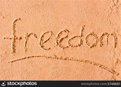 Freedom written on wet sand at the sea