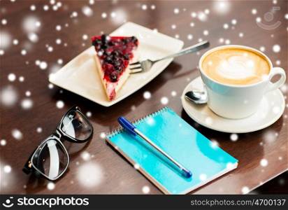 freelance and object concept - close up of notebook with pen, eyeglasses, coffee cup and berry cake on table over snow