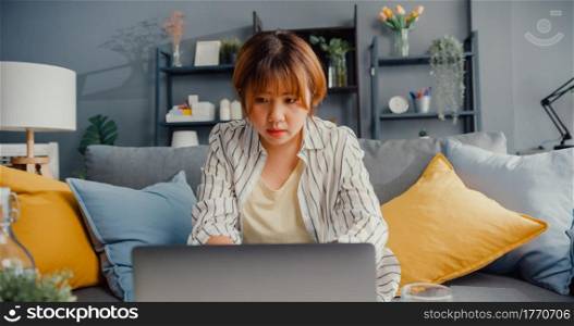 Freelance Asia lady casual wear using laptop online learning in living room at house. Working from home, remotely work, distance education, social distancing, quarantine for corona virus prevention.