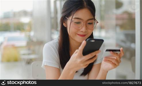 Freelance Asian women online shopping at coffee shop. Young Asia Girl using mobile phone, credit card buy and purchase e-commerce internet on table at outdoor cafe in the evening concept.