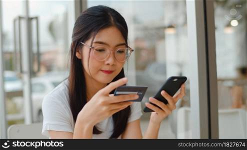 Freelance Asian women online shopping at coffee shop. Young Asia Girl using mobile phone, credit card buy and purchase e-commerce internet on table at outdoor cafe in the evening concept.