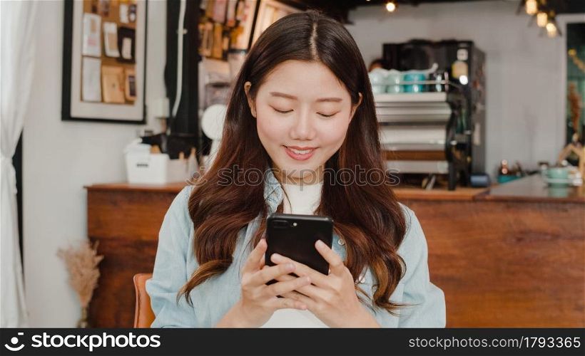 Freelance Asian women using mobile phone at cafe. Young Japanese Asian girl using smartphone checking social media on the internet on the table at coffee shop concept.