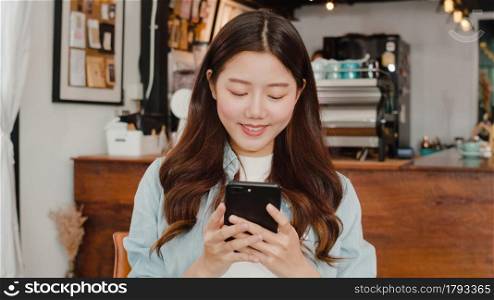 Freelance Asian women using mobile phone at cafe. Young Japanese Asian girl using smartphone checking social media on the internet on the table at coffee shop concept.