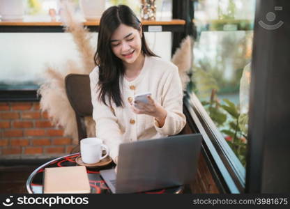freelance business beautiful positive smile young asian woman wearing warm clothes online working with message on smartphone with laptop computer and coffee cup mug at house in the living room or cafe