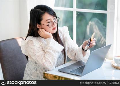freelance people business female think hard of debt to pay expenses holding a credit card working with laptop computer in coffee shop like the background,for online shopping and payment via internet.