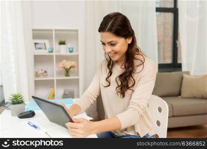 freelance, technology and education concept - happy smiling woman with tablet pc computer and notebook working or learning at home. student or freelancer with tablet pc at home