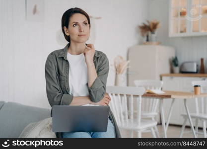 Freelancer is planning future and dreaming. Spahish woman is sitting in front of computer at home. Employee is working on project and thinking on ideas. Remote work on quarantine at cosy kitchen.. Freelancer is planning future and dreaming. Spahish woman is sitting at computer at cosy kitchen.