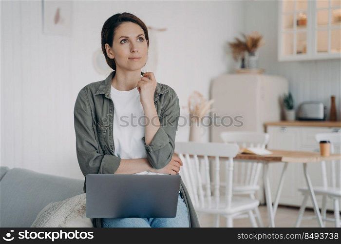 Freelancer is planning future and dreaming. Spahish woman is sitting in front of computer at home. Employee is working on project and thinking on ideas. Remote work on quarantine at cosy kitchen.. Freelancer is planning future and dreaming. Spahish woman is sitting at computer at cosy kitchen.