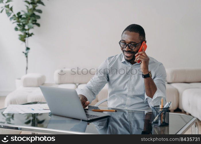 Freelancer is working online and having conversation with client on phone. Happy afro businessman has online meeting. Workplace at home office. Remote african american worker.. Freelancer is working online and having conversation or meeting with client on phone.