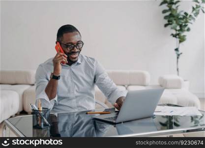 Freelancer is working online and having conversation with client on phone. Happy afro businessman has online meeting. Workplace at home office. Remote african american worker.. Freelancer is working online and having conversation or meeting with client on phone.