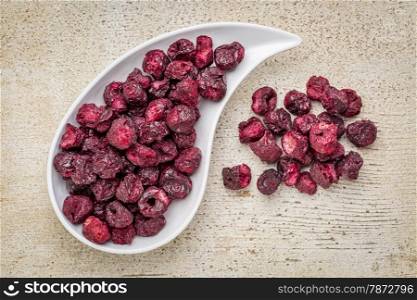 Freeze dried cherries in a teardrop bowl against rustic barn wood.