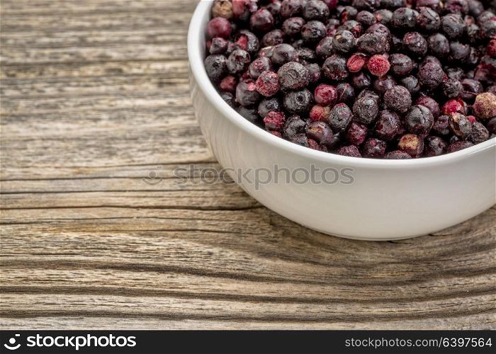 freeze dried elderberries in white, ceramic bowl against grained wood