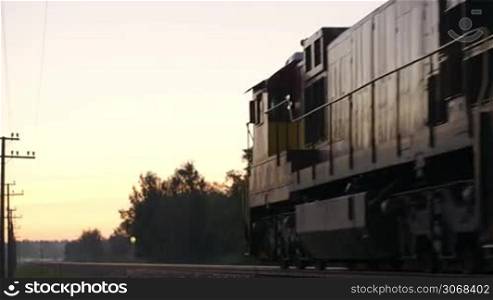 Freight train passing by slowly in the countryside at sunset. View of train going into the distance.