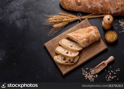 French baguette bread sliced on a wooden cutting board against a dark concrete background. Preparing the dinner table. French baguette bread sliced on a wooden cutting board against a dark concrete background