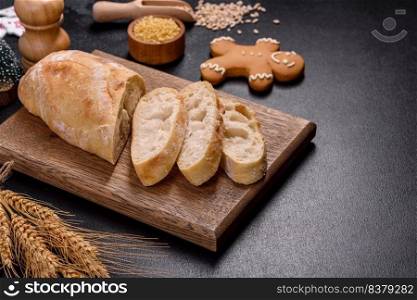 French baguette bread sliced on a wooden cutting board against a dark concrete background. Preparing the dinner table. French baguette bread sliced on a wooden cutting board against a dark concrete background