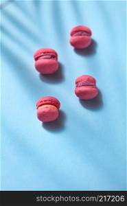 French cake macaroons on blue background with shadows from above, top view with copy space ,minimal concept.. Composition of pink colored macaroon on blue background, flat lay