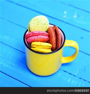 French cake made from egg white and almond flour macarons in a yellow ceramic cup on a blue wooden background, top view