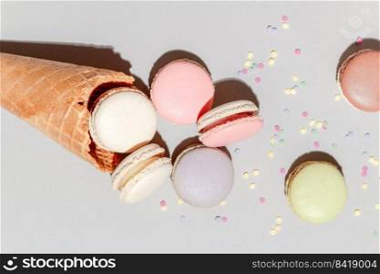 French dessert concept, Colorful macarons are served in waffle cone and falling on grey background.