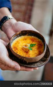 French dessert, Hands holding beautiful creamy vanilla Creme Brulee in coconut shell. Close up shot from side top