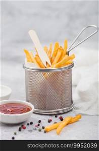 French fries chips in strainer basket with salt and tomato ketchup on light table background.