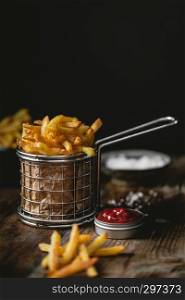 French fries in a basket with ketchup and salt on a dark background