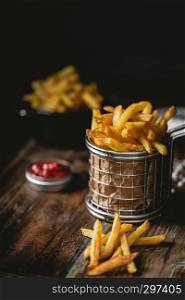 French fries in a basket with ketchup and salt on a dark background