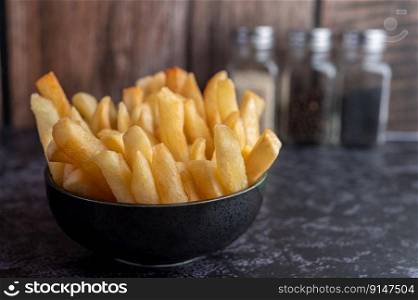 French fries in a black cup on the cement ground. Selective focus.