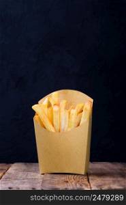 French fries in brown paper basket on wooden table with dark background copy space