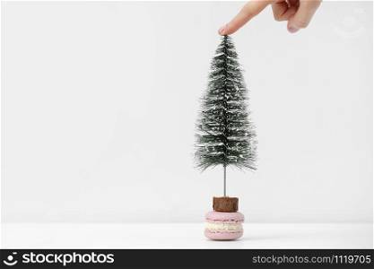 french macaroni or macaroon dessert on white table. Girl&rsquo;s hand holds a Christmas tree near dessert. Preparing for the Christmas holidays. french macaroni or macaroon dessert on white table. Girl&rsquo;s hand holds a Christmas tree near dessert. Preparing for the Christmas holidays.