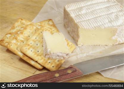 French pont l&rsquo;eveque cheese with biscuits and a knife on a chopping board,