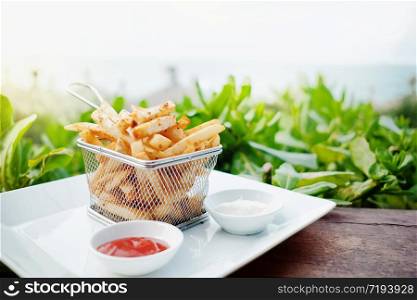French Potato Fries on Metal Mesh Flying Sieve with Two Dipping Sauce, Served on Rustic Wooden Table in Outdoor