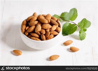 Fresh Almond nuts in a ceramics bowl on white wooden background