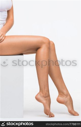 Fresh and beautiful. Attractive young woman in panties sitting on cube and touching perfect legs against white background. Woman with perfect legs