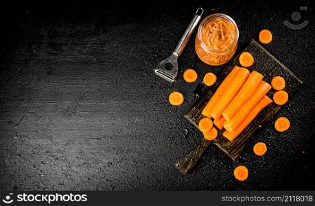 Fresh and canned carrots on a cutting board. On a black background. High quality photo. Fresh and canned carrots on a cutting board.