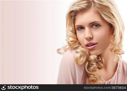 fresh and pretty young girl wearing a pink shirt and with curly hairstyle on her blond long hair and beautiful face looking at the camera with attractice pose against white background