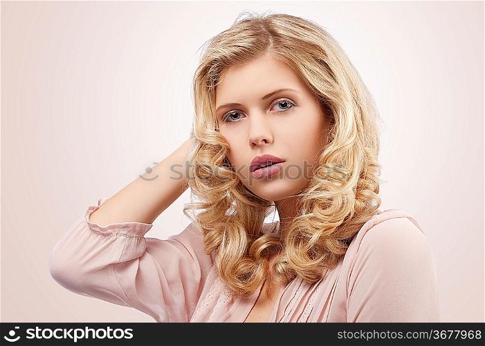 fresh and pretty young girl wearing a pink shirt and with curly hairstyle on her blond long hair looking at the camera with lovely pose against white background
